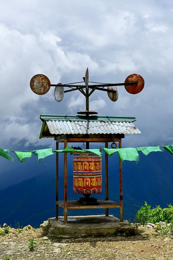 A prayer wheel under a small roof with prayer flags