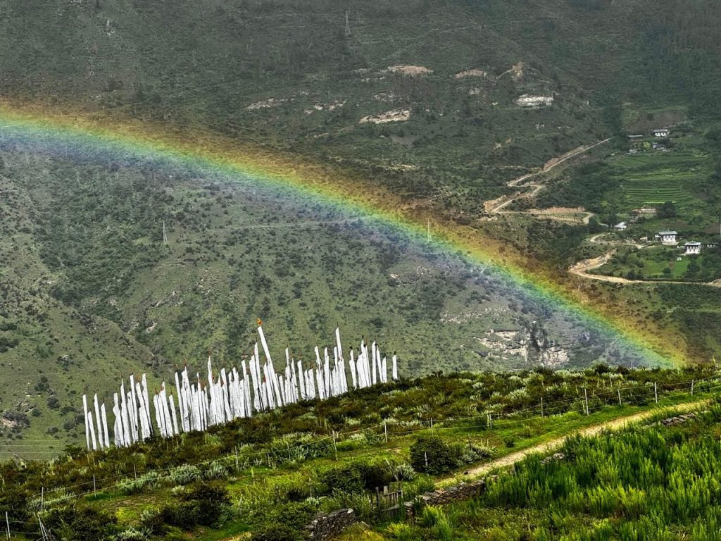 A rainbow over white prayer flags near The Happiness Farm